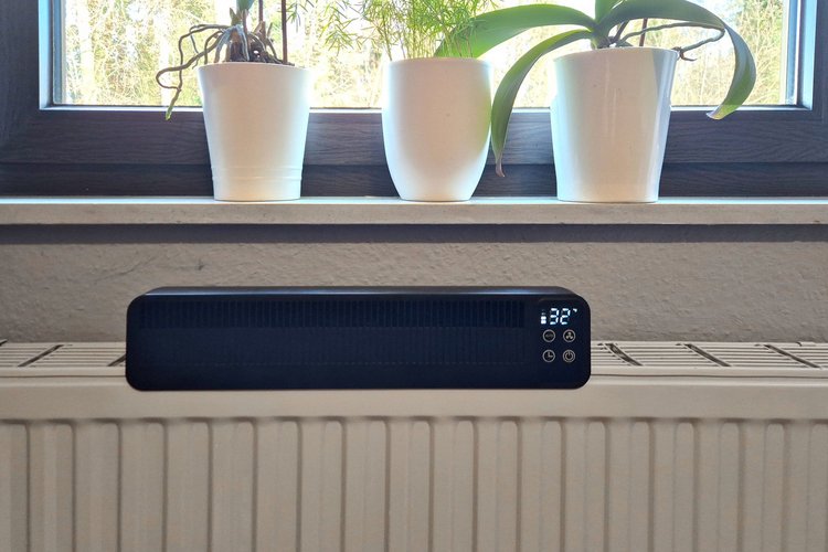 Heizkörperventilator auf Heizung Ein schwarzer Heizkörperventilator auf einer Heizung, er zeigt die Temperatur "32°" an, im Hintergrund eine Fensterbank mit Töpfen.