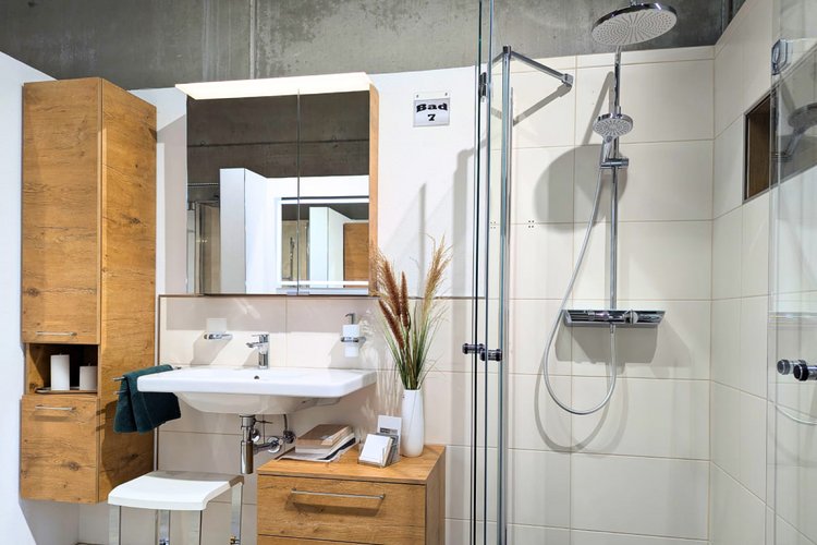 Modernes Badezimmer mit Holzmöbeln, ebenerdiger Dusche, großem Spiegel und Waschbecken vor weiß gefliester Wand.