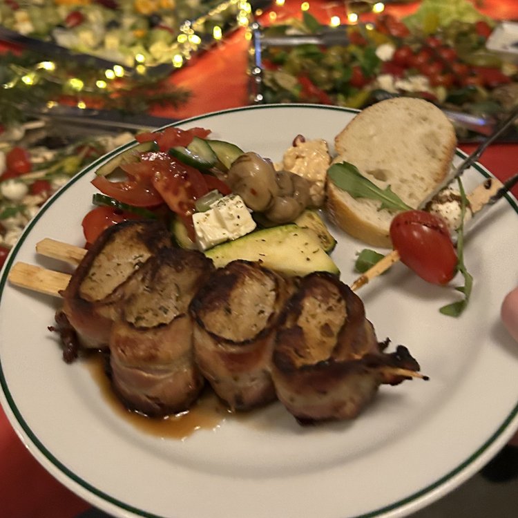 Ein Mitarbeiter von Team Hörmann hält auf der Weihnachtsfeier einen Teller mit verschiedenen Speisen, im Hintergrund ein großes Buffet.