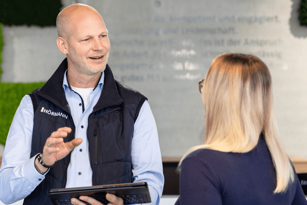 Beratungsgespräch bei Hörmann mit Tablet-Unterstützung Mann in Hörmann-Weste spricht mit einer Frau und hält dabei ein Tablet.