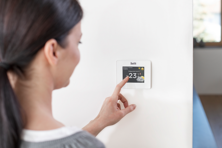 Frau bedient ein modernes Smart-Home-Thermostat an der Wand zur Steuerung der Raumtemperatur.