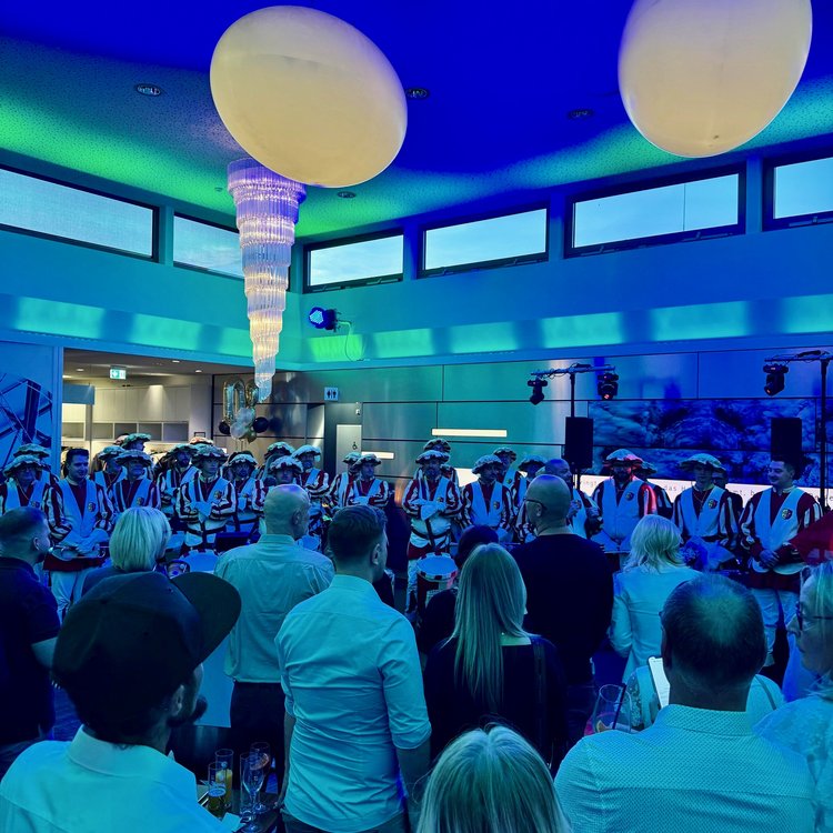 Große Menschenmenge bei einer Veranstaltung in modernem Saal mit Bühnenlicht, runden Leuchtelementen und gehobener Atmosphäre.