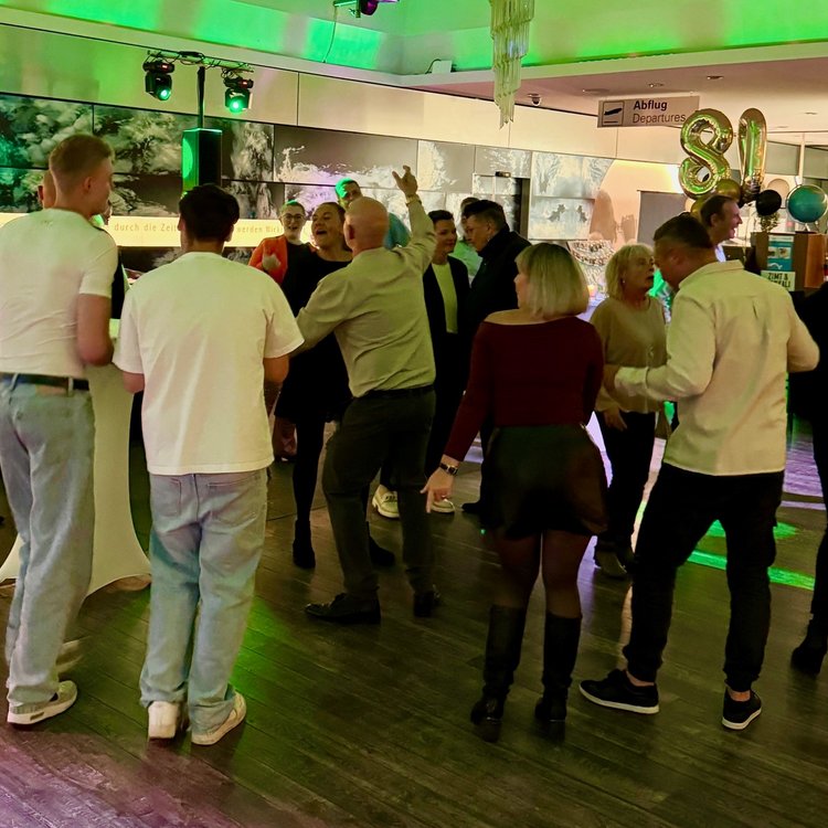 Menschen tanzen und unterhalten sich in lockerer Atmosphäre bei einer Veranstaltung mit grüner Lichtstimmung.