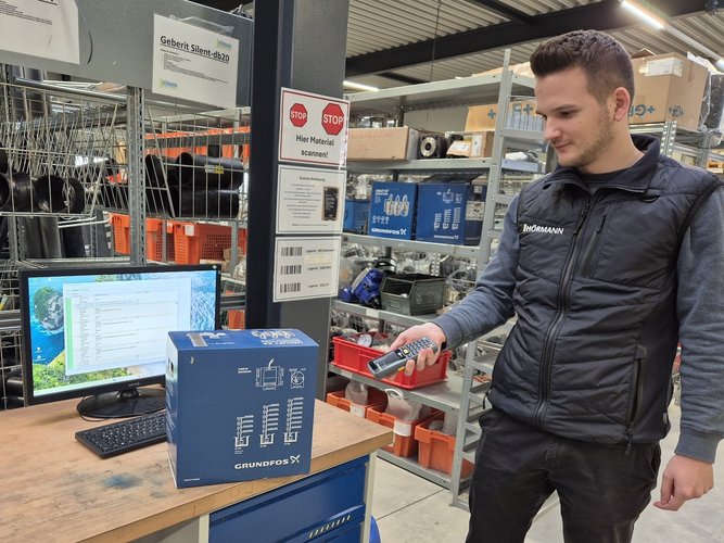 Ein Mitarbeiter von Team Hörmann scannt ein Paket im digitalen Lager mit einem Handscanner.