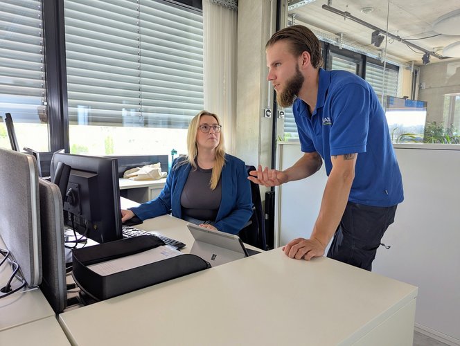 Natalie Götz von Team Hörmann arbeitet am Schreibtisch und spricht mit einem Kollegen