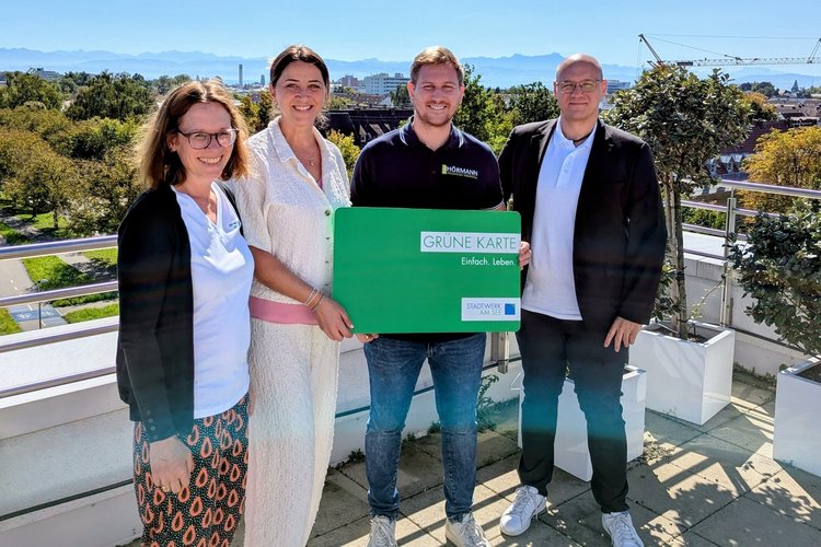 Mitarbeiter von Team Hörmann und dem Stadtwerk am See halten gemeinsam die Grüne Karte in der Hand, im Hintergrund der Blick auf Alpen und Bodensee.