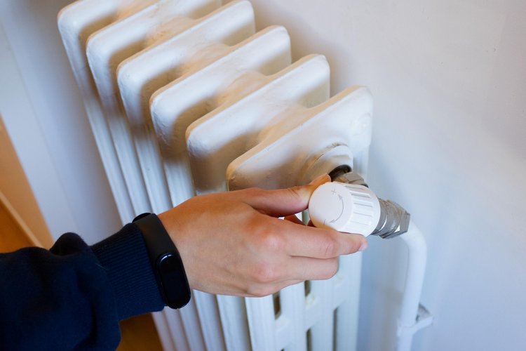 Hand dreht das Thermostat an einem weißen Heizkörper zur Temperaturregelung.