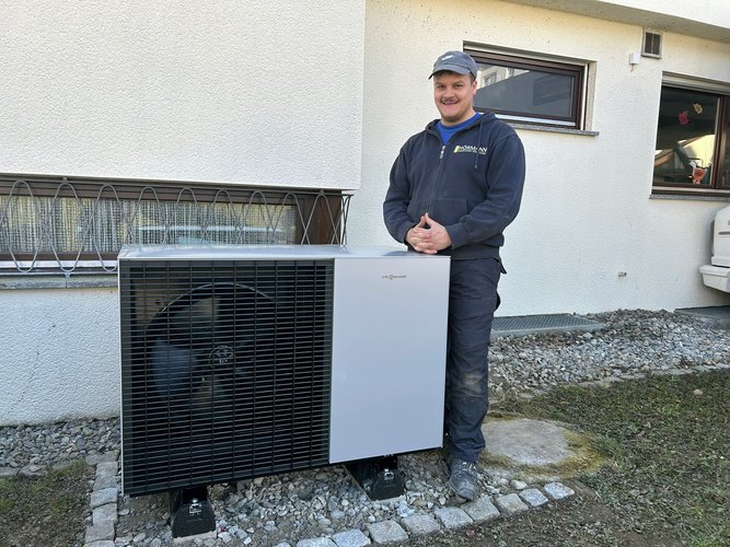 Mitarbeiter von Team Hörmann steht neben Wärmepumpe vor Wohnhaus.
