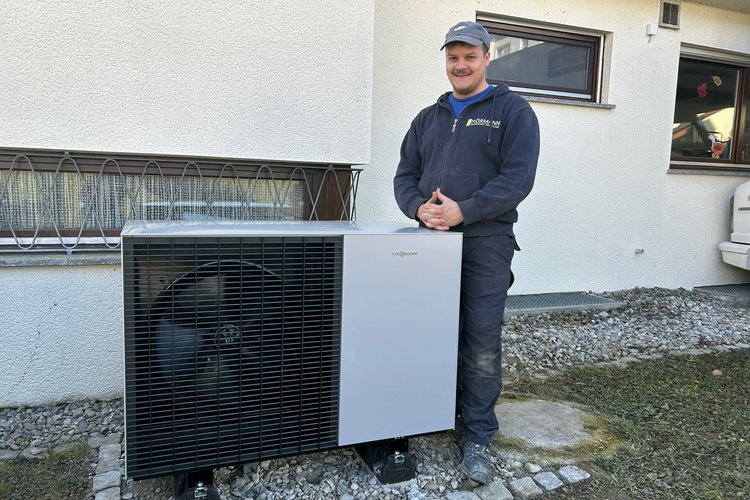 Mitarbeiter von Team Hörmann steht neben Wärmepumpe vor Wohnhaus.