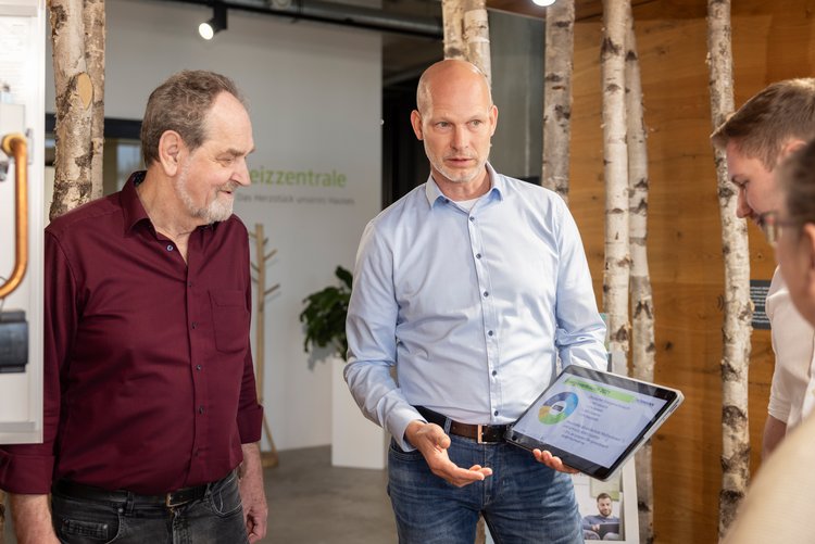 Beratungsgespräch mit Tablet-Präsentation Zwei Männer präsentieren einer Gruppe eine technische Zeichnung oder Planung auf einem Tablet in modernem Beratungsumfeld.